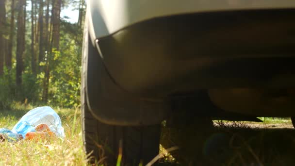 Una bolsa azul con botellas de plástico de basura se encuentra en la naturaleza cerca del coche, la contaminación de la naturaleza por residuos de plástico, basura y un coche, basura — Vídeos de Stock