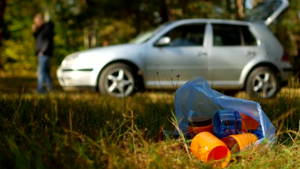 Çöp plastik şişe ile bir paket doğa üzerinde yatıyor, arka planda bir araba var ve insanlar, doğa kirliliği plastik atık, Doğa ve çöp, bir araba ile bi boka yaramaz yürüyor — Stok video