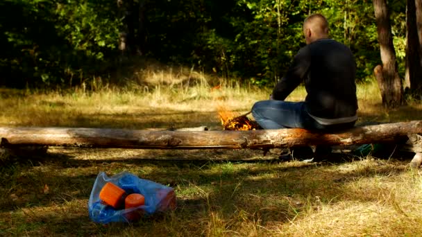 Een pakket met plastic afval ligt op een glade, een vuur verbrandt, mensen lopen in de achtergrond, camping en natuur vervuiling, afval, geplateerde — Stockvideo