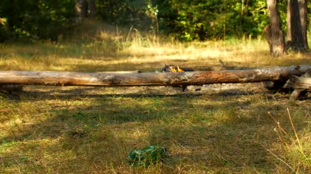 Ein Mann schlägt in der Natur mit dem Fuß auf eine liegende Flasche, Nahaufnahme, im Hintergrund brennt ein Feuer, Erholung im Freien — Stockvideo