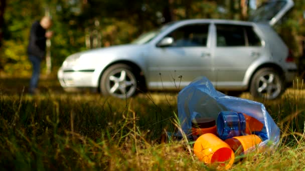 Un paquete de basura con botellas de plástico se encuentra en la naturaleza, en el fondo hay un coche y la gente está caminando, la contaminación de la naturaleza con residuos de plástico, un coche en la naturaleza y la basura, basura — Vídeos de Stock