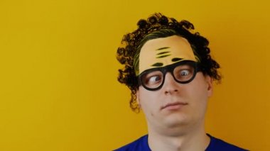 Şaşılık ile deli kıvırcık adam döner ya da onun gözleri, siyah saçlar, çılgın ve neşeyle insan duygu, sarı duvar arka plan üzerinde rulo