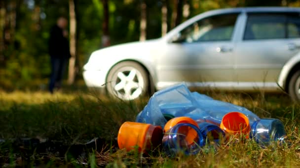 Çöp plastik şişe ile bir paket doğa üzerinde yatıyor, arka planda bir araba var ve insanlar, doğa kirliliği plastik atık, Doğa ve çöp, bir araba ile bi boka yaramaz yürüyor — Stok video