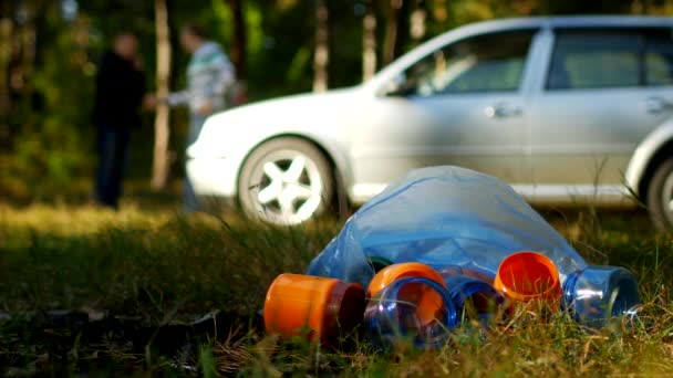 Ein Paket Müll mit Plastikflaschen liegt in der Natur, im Hintergrund steht ein Auto und die Menschen laufen, die Natur verschmutzt mit Plastikmüll, ein Auto in der Natur und Müll, Müll — Stockvideo