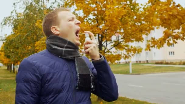 Ill or sick man uses spray aerosol against a sore throat due to Influenza flu virus in the city or outdoor in the autumn or fall — Stock Video