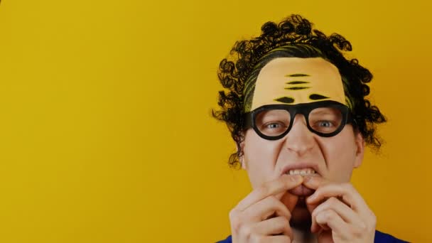 Insane man holds his tongue by his fingers, curly black hairs, funny cheerfully human emotions, on yellow wall background — Stock Video