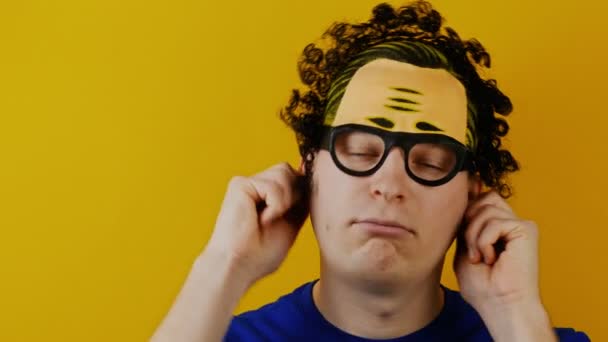 Kudrnatá šílenec sám tahá za uši a ukazuje jeho jazyk, legrační, vesele, lidské emoce, na pozadí žluté zdi, černé vlasy — Stock video