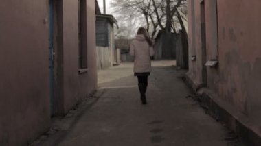 Bir ceket uzun saçlı bir kız bir dar kentsel sokak, kentsel, uyuşuk, dar sokakta yürüyor.