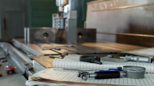 Частная мастерская по работе с металлическими деталями, на заднем плане буровая установка сверлит отверстие в шкиве, на столе лежат измерительные приборы — стоковое видео