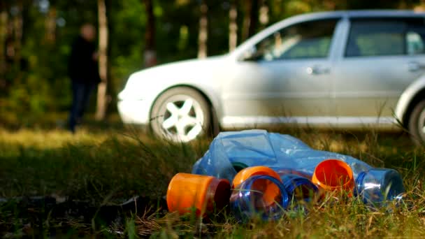 Ein Paket Müll mit Plastikflaschen liegt in der Natur, im Hintergrund steht ein Auto und die Menschen laufen, die Natur verschmutzt mit Plastikmüll, ein Auto in der Natur und Müll, Müll — Stockvideo