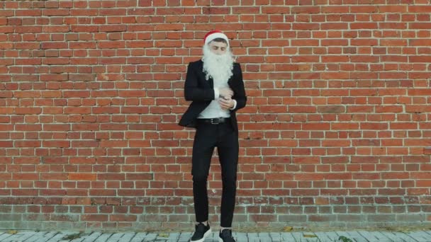 白胡子和圣诞老人克劳斯帽子的男子穿着黑色西装 夹克和白衬衫 圣诞快乐 2019年新年 红砖墙为背景 — 图库视频影像