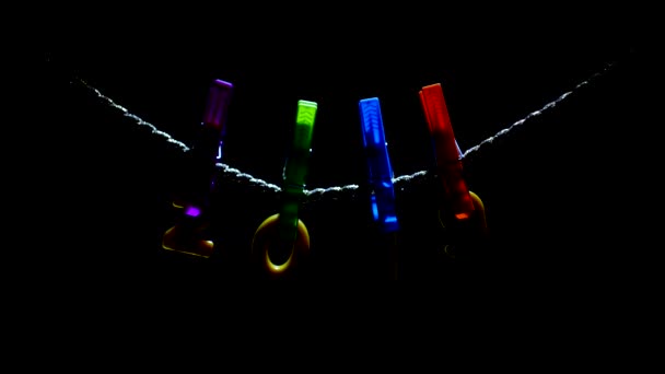 Figures 2019 accroché sur des pinces à linge et une corde sur un fond noir qui rétro-éclairera, gros plan, multicolore, Noël, heureux — Video