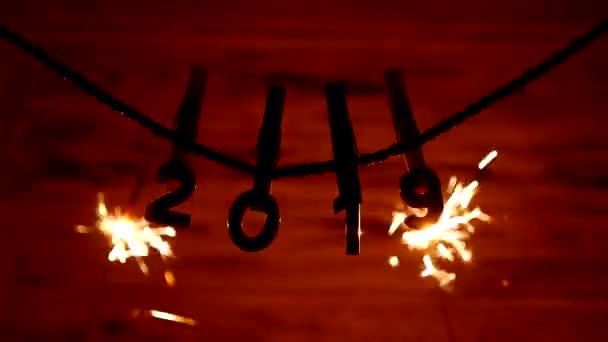 Siffror 2019 hängande på klädnypor och rep, tomtebloss bränning i bakgrunden, nytt år 2019, jul, nyår, gnista — Stockvideo
