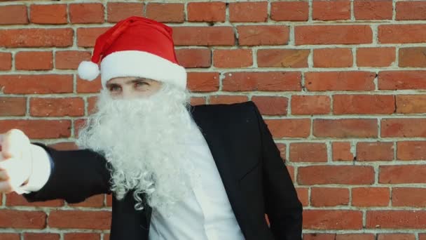Hombre como un Santa Claus elige y muestra con su dedo índice a la cámara, Feliz Navidad y Año Nuevo 2019, pared de ladrillo rojo como fondo — Vídeos de Stock