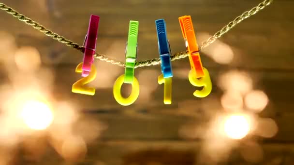 Gelbe Ziffern 2019 hängen an einer Wäscheklammer an einem Seil auf einem hölzernen Hintergrund, Nahaufnahme, Neujahr 2019, Weihnachten, sie sind Benzal, Funken, — Stockvideo