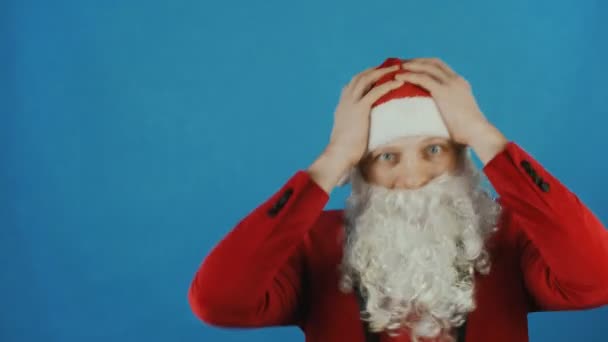 Karácsonyi és újévi 2019, mint a Santa ember meglepett, és tartja a fejét a kezében, a kék háttér — Stock videók