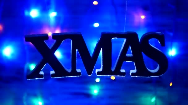 Christmas inscription XMAS freely dangles in the air, on a wooden background, new year lights, new year holidays, new year 2019, Christmas — Stock Video