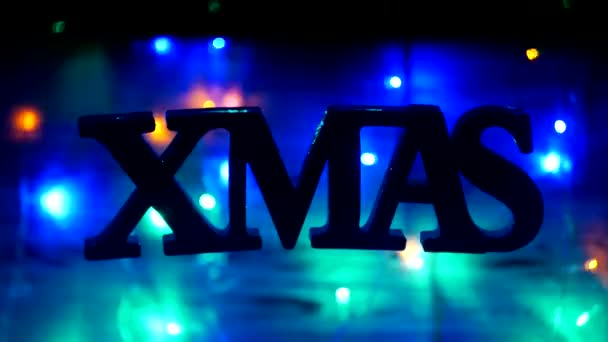 Kerst inscriptie Xmas bungelt vrij in de lucht, op een houten achtergrond, Nieuwjaar lichten, Nieuwjaars vakantie, Nieuwjaar 2019, Kerstmis, achtergrond — Stockvideo
