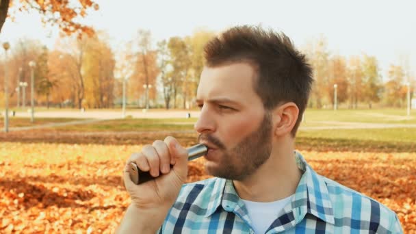 Skäggig man inhalerar ånga av en e-cigarett och blåser ett moln av ånga — Stockvideo