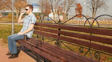 moda adam bir bankta oturur, bir e-sigara içiyor ve kahve içer