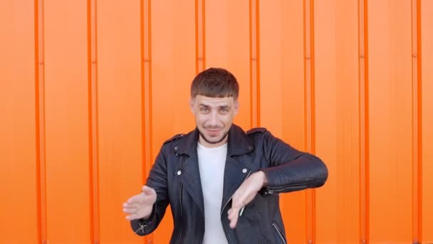 Young positive male brunette in a black jacket is dancing on an orange background, close-up, caucasian, slow motion — Stock Video