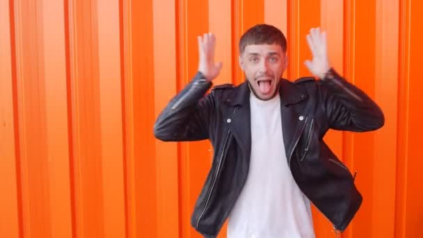 Young caucasian positive and emotional man clutches his head, is surprised and shows his tongue on an orange background, close-up, slow motion, grimaces — Stock Video