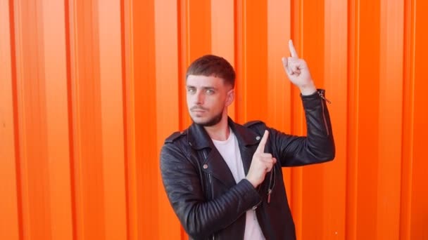 Молодой кавказский веселый брюнетка мужчина в черной кожаной куртке танцует на оранжевом фоне, крупным планом, замедленной съемки, скачки — стоковое видео