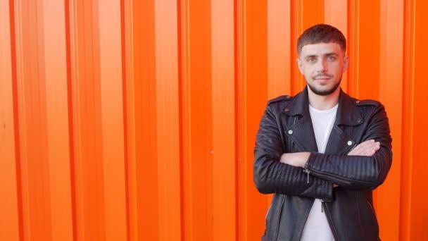Young kind and cute man with a beard folded his arms crosswise looking into the camera on an orange background, close-up, copy-space, slo-mo — Stock Video