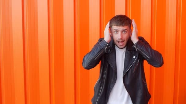 Emotional guy is surprised and holding his head, fear, facial expressions, orange background, slow motion — Stock Video