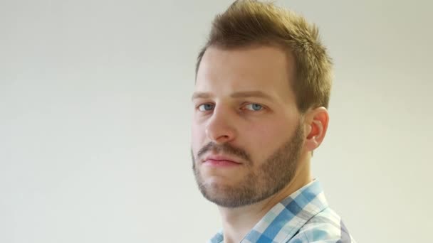 Serious and brutal man with a beard turns his head and looks into the camera on a white background, close-up, copy space, caucasian — Stock Video