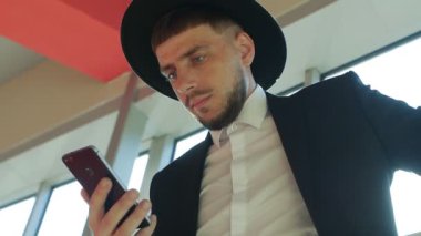 Bir çanta ve şapkası sakallı şık beyaz erkek işadamı duran ve bir akıllı telefon İşletme Merkezi, yakın çekim, Güneş, slo-mo bölümündeki bilgileri okuduktan