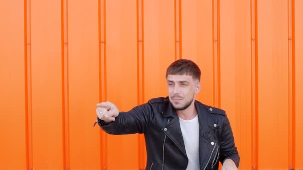 Caucasian young positive and emotional male brunette in a black jacket dancing against an orange background, close-up, slow-mo, lifestyle — Stock Video