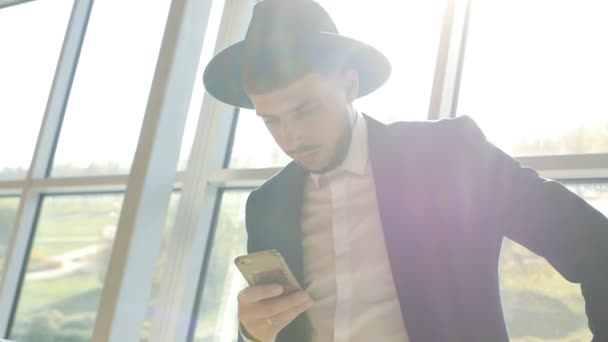 Stijlvolle Kaukasische man in zwart pak en hoed telefoon in zijn hand houdt en Lees informatie terwijl ze op de luchthaven, close-up, slo-mo, mobiele telefoon — Stockvideo