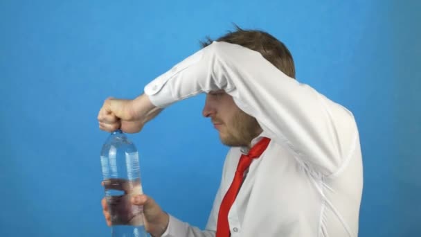 Un uomo caucasico con la barba in camicia bianca e cravatta da sbornia apre una bottiglia di acqua minerale e bevande, dipsomane, fondo blu — Video Stock