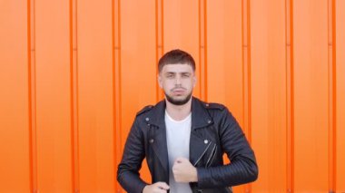 Beyaz genç olumlu ve duygusal erkek esmer dans bir turuncu arka plan, yakın çekim, uyuşuk karşı siyah ceket
