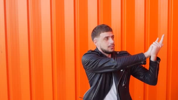 Giovane uomo caucasico bruna che gioca con una pistola immaginaria su uno sfondo arancione, primo piano, rallentatore — Video Stock
