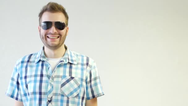 Young stylish unshaven caucasian man in black glasses is standing smiling and looking at the camera, close-up, white background, copy space, fashionable — Stock Video