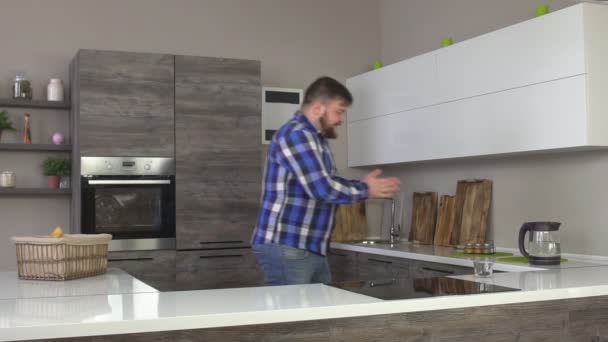 Довольный и радостный кавказский мужчина с бородой входит в современную кухню и делает себе черный кофе, замедленное движение — стоковое видео