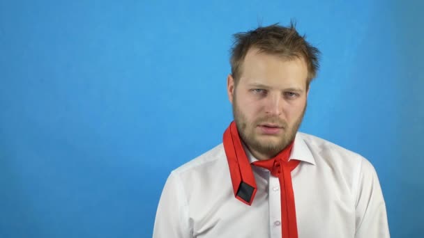 Young drunk caucasian man in white shirt and tie looks into the camera and staggers, copy space, hangover, blue background — Stock Video