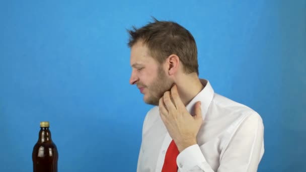 Un homme caucasien avec une gueule de bois avec une barbe ouvre avec gourmandise une bouteille de bière et la boit, avide d'alcool, de sécheresse, de fond bleu — Video