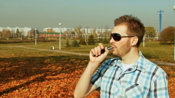 Skäggig man inhalerar ånga av en e-cigarett och blåser ett moln av ånga — Stockvideo