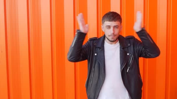 Young caucasian positive and emotional man clutches his head, is surprised and shows his tongue on an orange background, close-up, slo-mo, grimaces — Stock Video