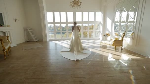 A noiva bonita em um vestido com um trem está em um estúdio branco, câmera lenta, visão traseira, casamento, glamour — Vídeo de Stock
