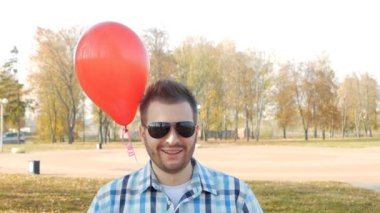 bir tür moda genç siyah gözlük standları ile kırmızı bir balon ve gülümsüyor, bir festival sürpriz, ağır çekim, kopyalama alanı