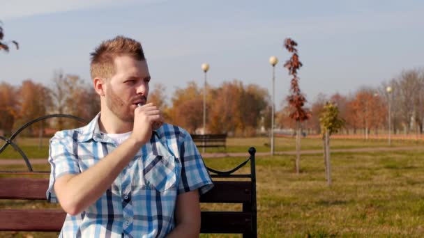 Jonge modieuze en knappe man met een baard zit op een bankje en rookvrije vape, close-up, kopieer ruimte, lifestyle, blijdschap — Stockvideo