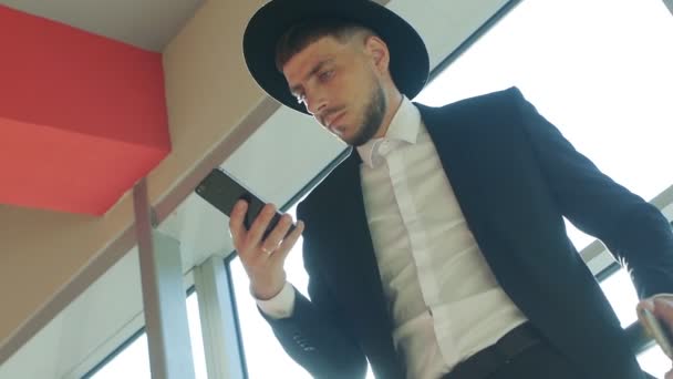 Kaukasische man reiziger in een hoed permanent op het station en op zoek naar de telefoon, close-up, slow-mo — Stockvideo