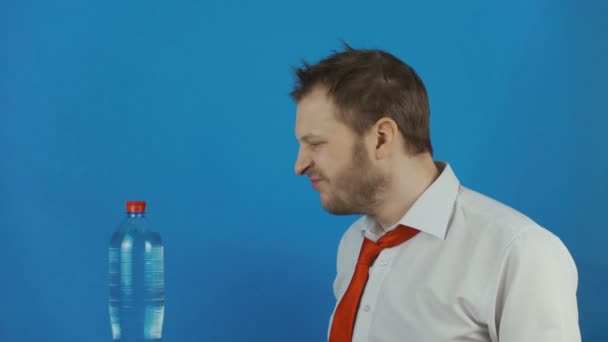 Hombre sin afeitar es un hombre de negocios sediento y descuidado con la boca seca mira una botella de agua y quiere beberla — Vídeos de Stock