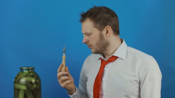 Careless man with can opener looks at closed jar of pickled cucumbers due to hangover after alcohol party — Stock Footage Careless man with can opener looks at closed jar of pickled cucumbers due to hangover after alcohol party Royalty Free Stock Footage