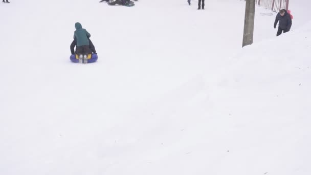 БОБРУЙСК, БЕЛАРУС - 6 ЯНВАРЯ 2019 года: Ребенок с отцом едут зимой с заснеженной горы на канате, медленное время — стоковое видео