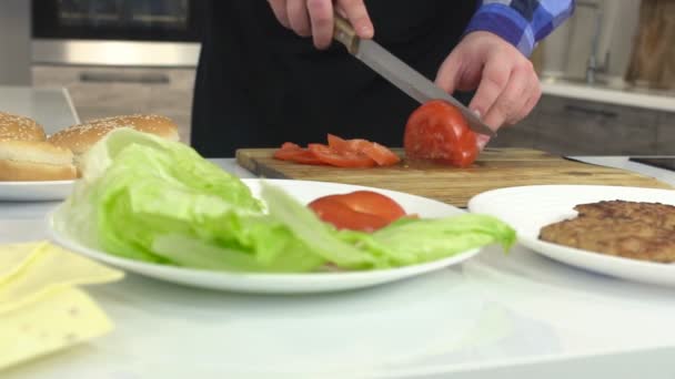 Un uomo in grembiule in cucina affetta un pomodoro in un piatto, al rallentatore, professionale, primo piano — Video Stock